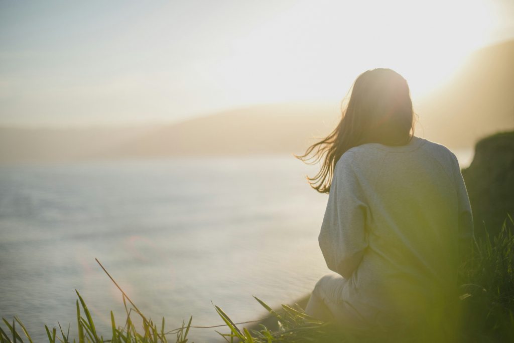 a woman sitting on a bank looking towards the ocean by artem-kovalev-fk3XUcfTAvk-unsplash